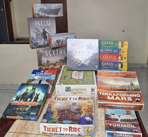A stack of board games on the family game table, including Scythe, Catan, Brass Birmingham, Carcassonne, Terraforming Mars, Ticket to Ride, Pandemic and Twilight Struggle.